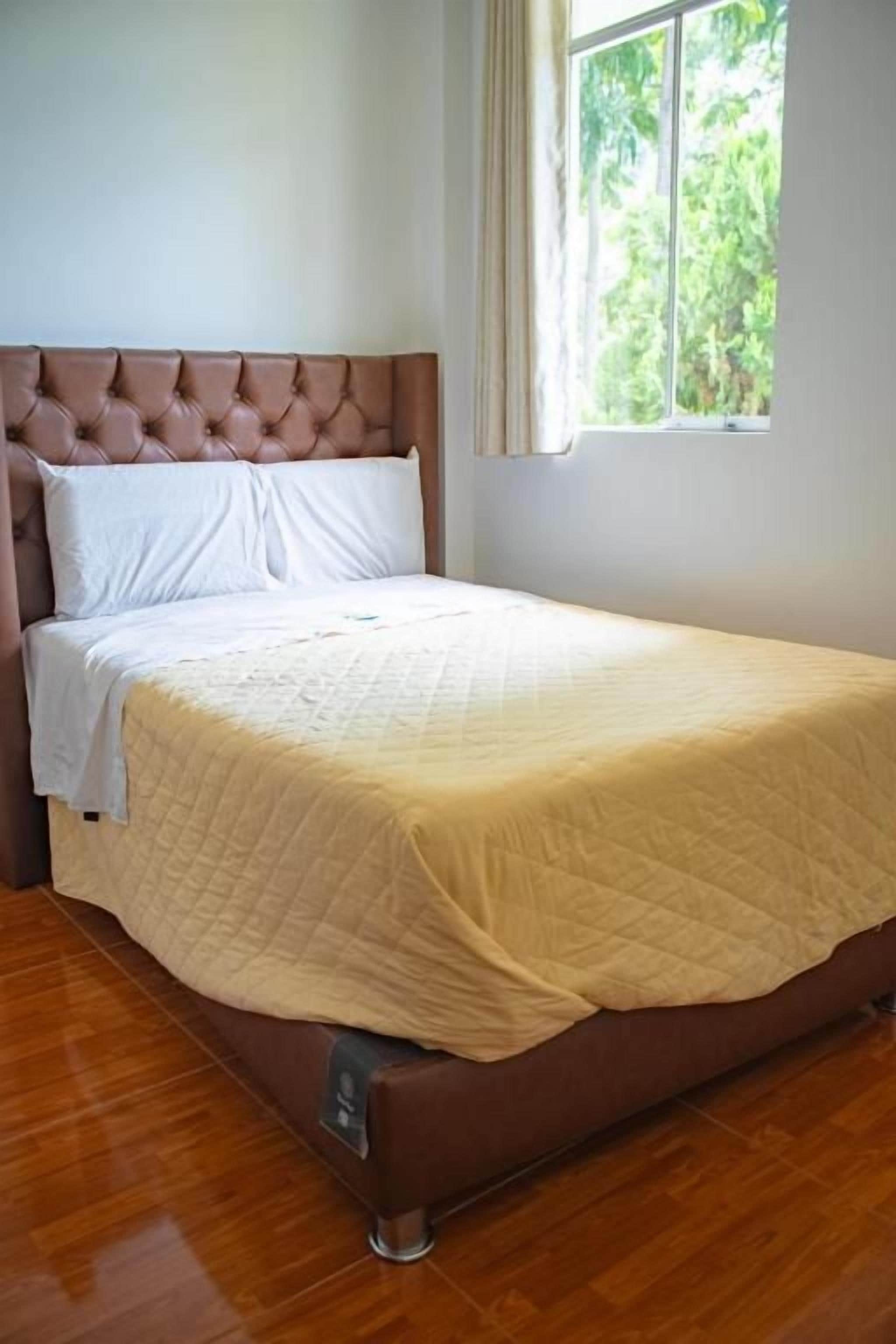 Uma cama de solteiro com cabeceira, uma janela com cortinas e piso de madeira.