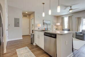 A modern kitchen with a central island, overhead pendant lights, and a ceiling fan. - The Magnolia on Prince | King Bed + Patio (Athens)
