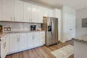 A modern kitchen with white cabinets, a stainless steel refrigerator, and a coffee maker on the countertop. - The Magnolia on Prince | King Bed + Patio (Athens)