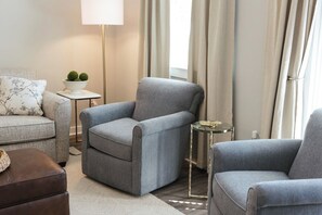 A modern living room with a grey armchair, a sofa, a small side table with a plant, and a lamp. - The Magnolia on Prince | King Bed + Patio (Athens)