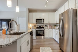 A modern kitchen with white cabinets, stainless steel appliances, and a granite countertop. - The Magnolia on Prince | King Bed + Patio (Athens)