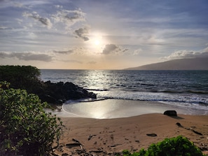 Una platja amb mar tranquil·la, riba rocosa i vegetació.
