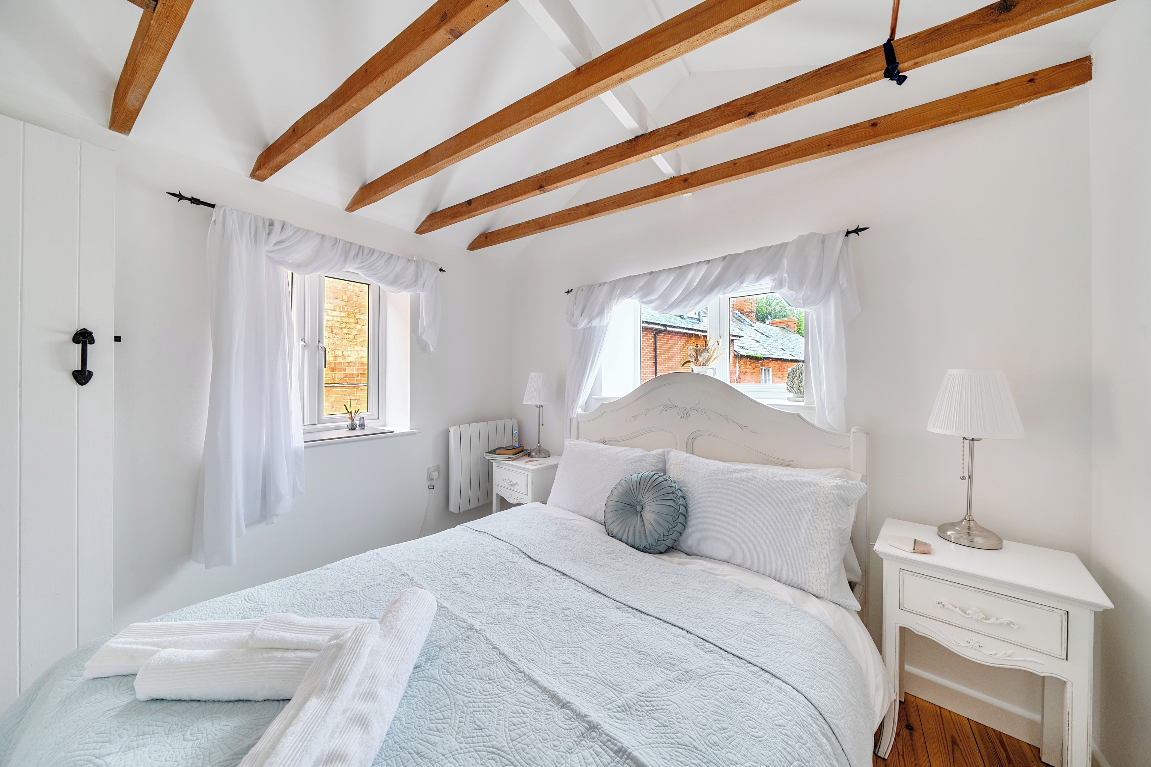 Una camera da letto con un letto, comodini, una finestra e travi in legno al soffitto.