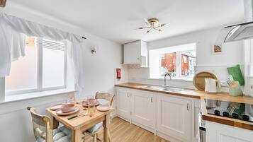 Een keuken met witte kastjes, een houten aanrecht, een eettafel met roze borden en een raam met uitzicht op gebouwen.