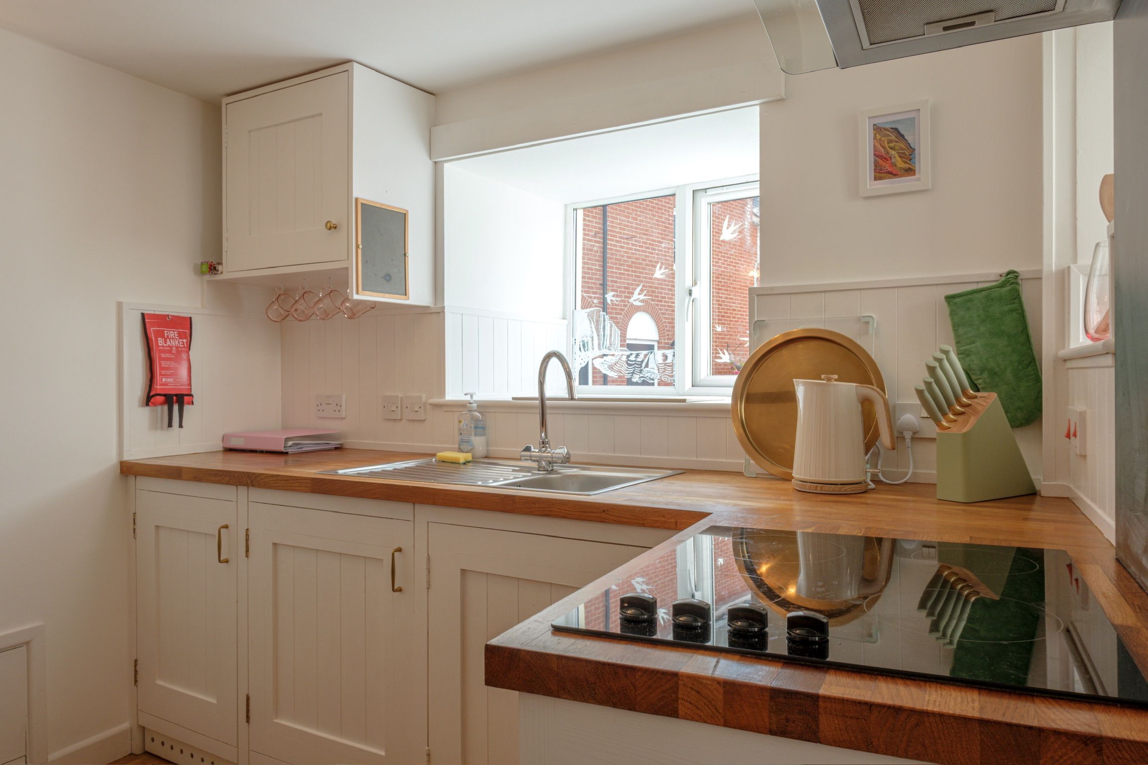 Una cocina con armarios blancos, encimera de madera, pileta de acero inoxidable y ventana con vista a un edificio de ladrillo.