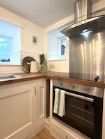 Una cocina compacta con horno integrado, extractor de acero inoxidable y ventana sobre el lavamanos.