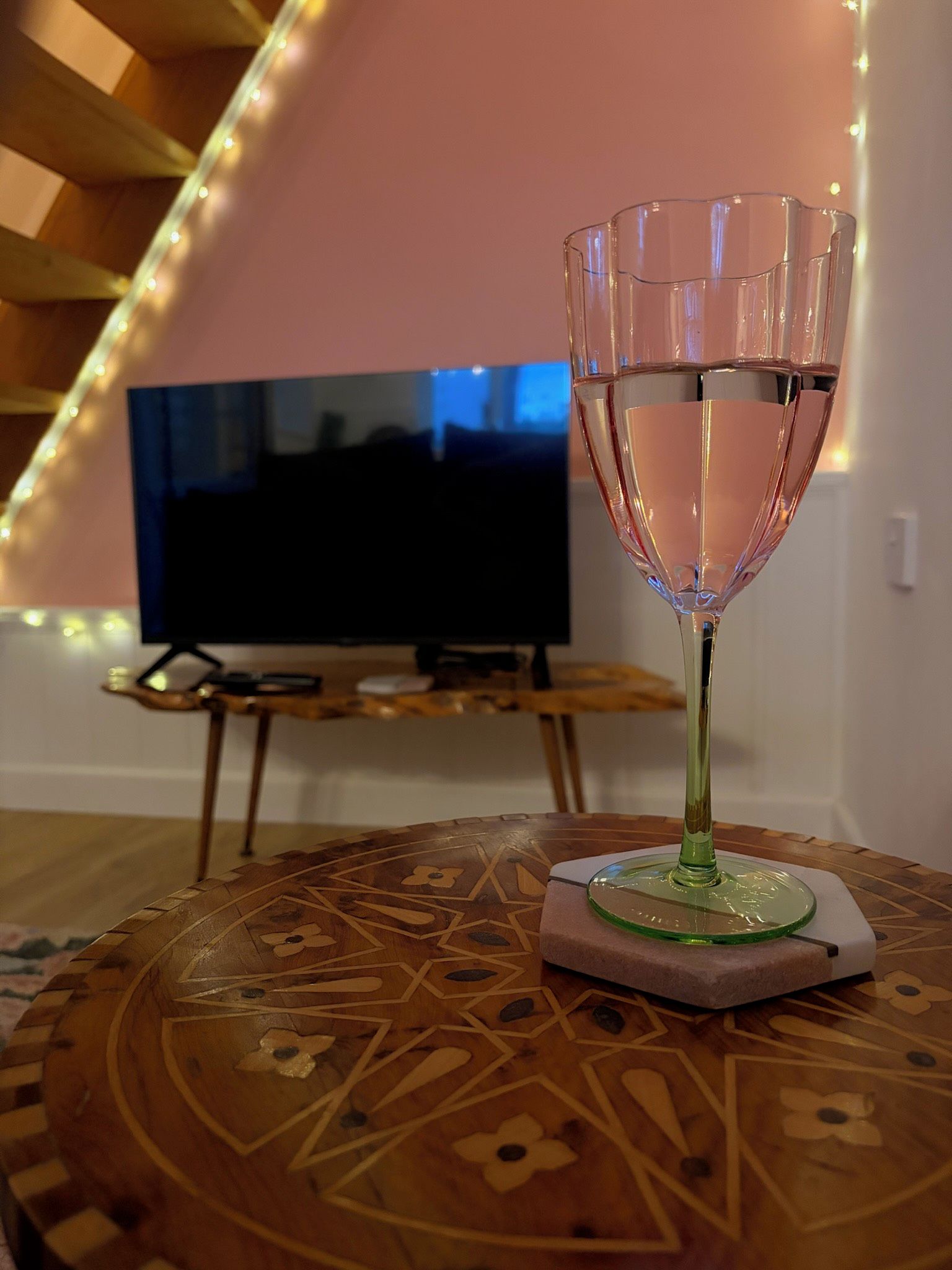 A glass of water on a coaster in a room with a TV and string lights.
