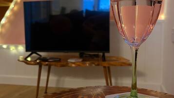 A glass of water on a coaster with a geometric pattern, a television in the background, and a staircase with string lights.