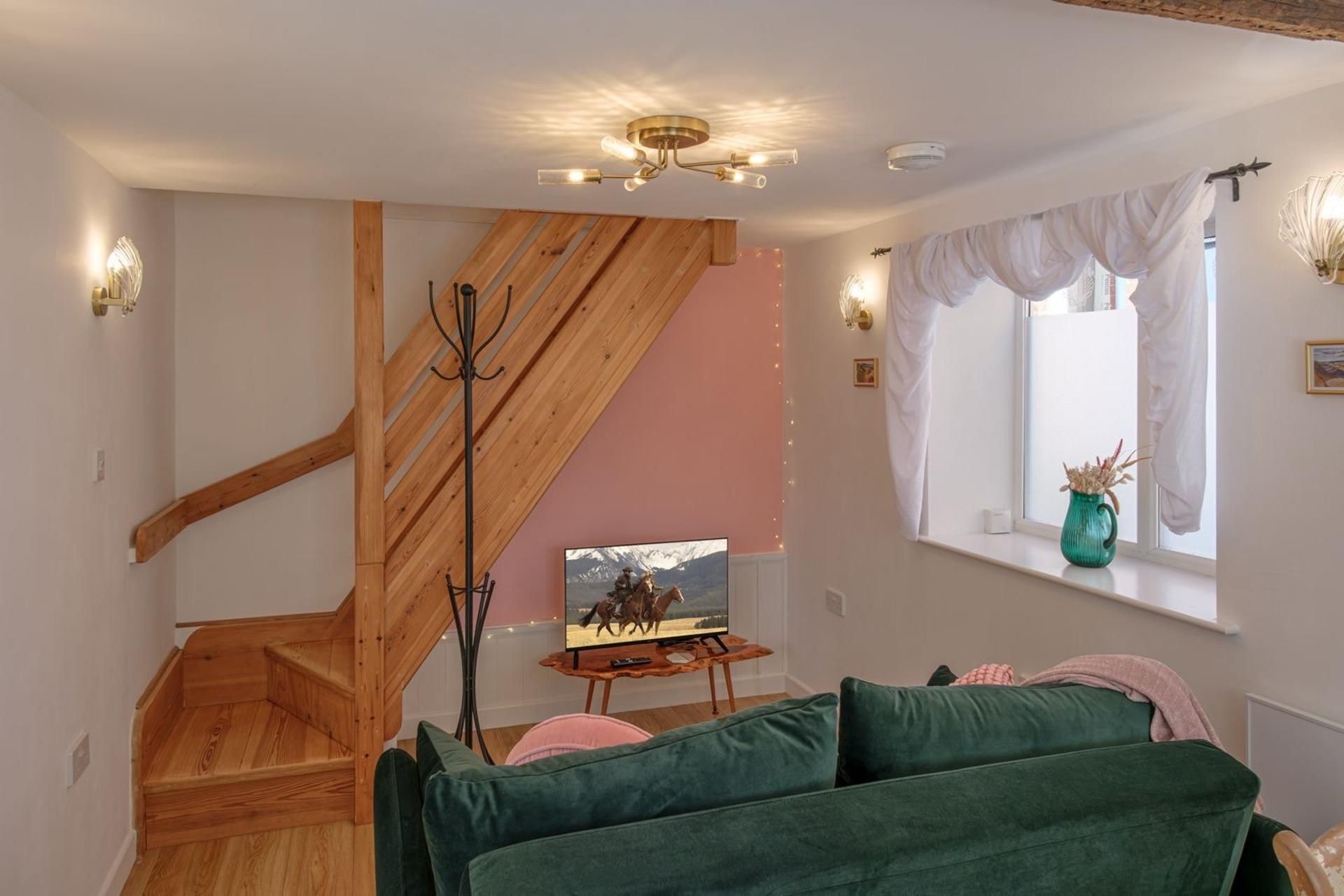 Een woonkamer met een houten trap, een groene bank, een televisie en een raam met gordijnen.