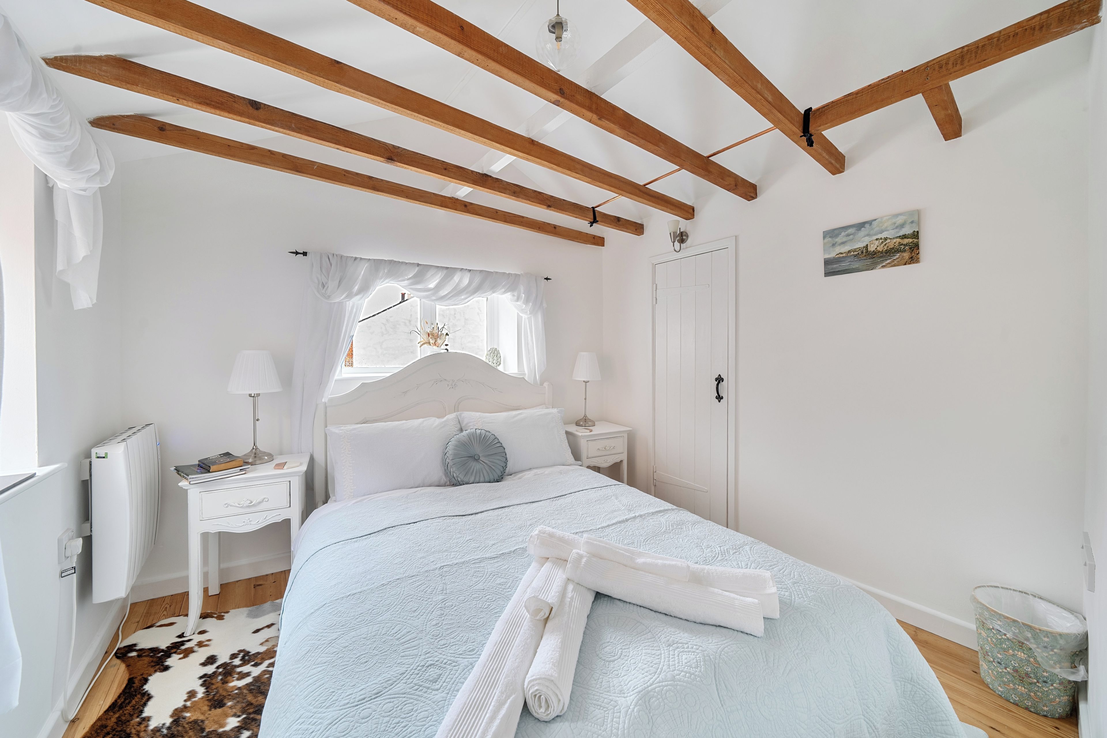 Een slaapkamer met een bed, nachtkastjes, een raam met gordijnen, een radiator en een deur.