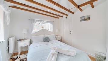 Een slaapkamer met een bed, nachtkastjes, een raam met gordijnen, een radiator en een deur.