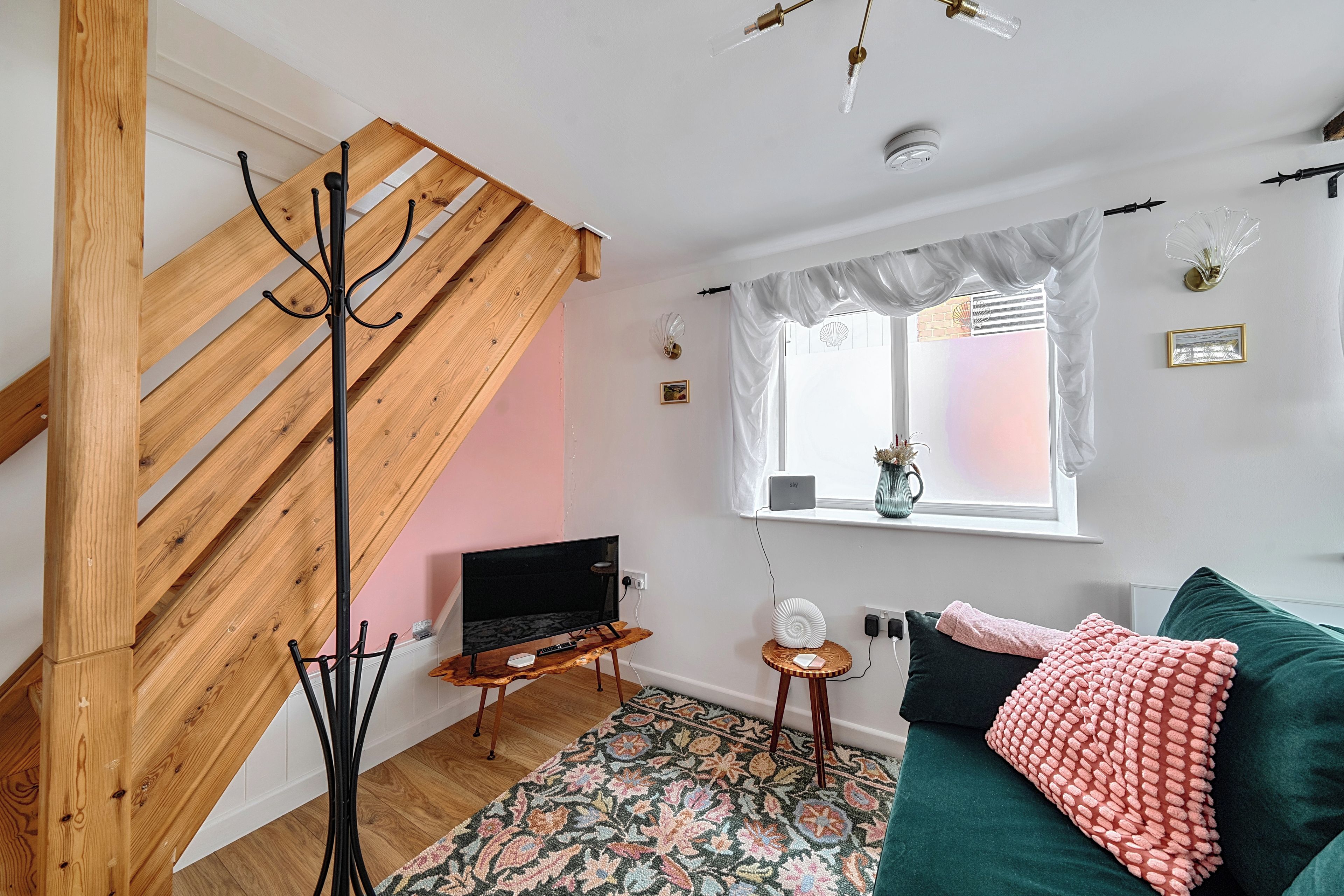 Una sala de estar moderna con una escalera de madera, un televisor de pantalla plana, un sofá verde y una alfombra estampada.