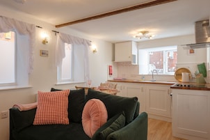 Una sala de estar acogedora con un sofá verde, una cocina con armarios blancos y un comedor con una mesa dispuesta para dos.