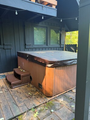 Uma banheira de hidromassagem com degraus, rodeada por um deck de madeira e uma área coberta com janelas.