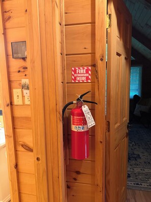 A wooden door with a fire extinguisher mounted on it, a fire exit sign, and a small plaque. - Cozy Cabin Nestled on Infamous Ski Mountain Rd. (Gatlinburg)