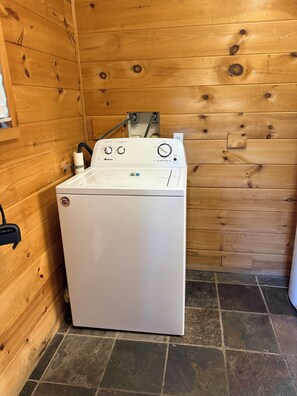 A white front-loading washing machine in a wooden room with a tiled floor. - Cozy Cabin Nestled on Infamous Ski Mountain Rd. (Gatlinburg)