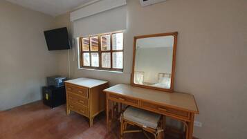 A room with a desk, a chair, a television mounted on the wall, and a window with blinds.