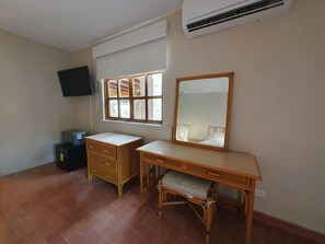 Quarto com escrivaninha, cadeira, televisão na parede e janela com persianas.
