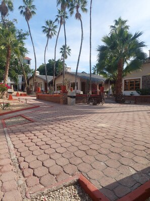 A courtyard with hexagonal paving, palm trees, and buildings with thatched roofs. - Sandy Shores 2A (La Paz)
