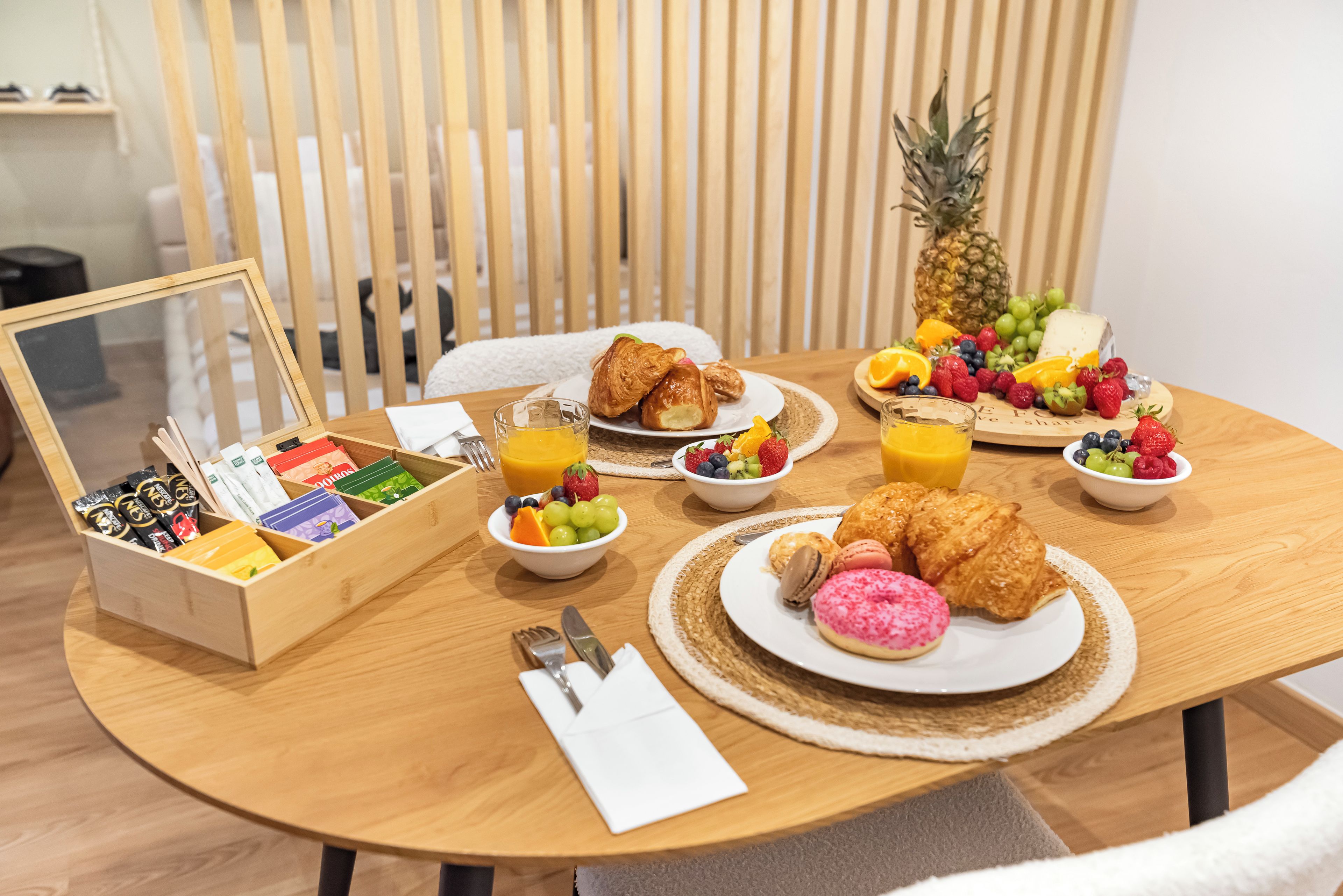 A breakfast setting with croissants, fruit, and a pineapple on a wooden table.
