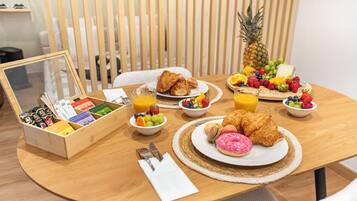 A breakfast setting with croissants, fruit, and a pineapple on a wooden table.