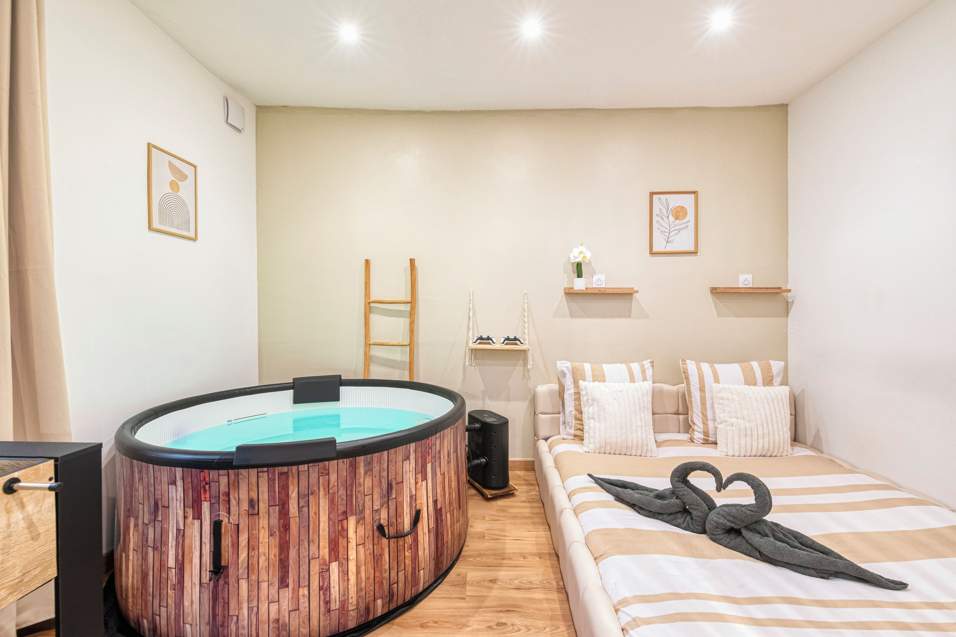 Een kamer met een houten jacuzzi, een bed met gestreepte beddengoed en een kleine tafel met een speaker.