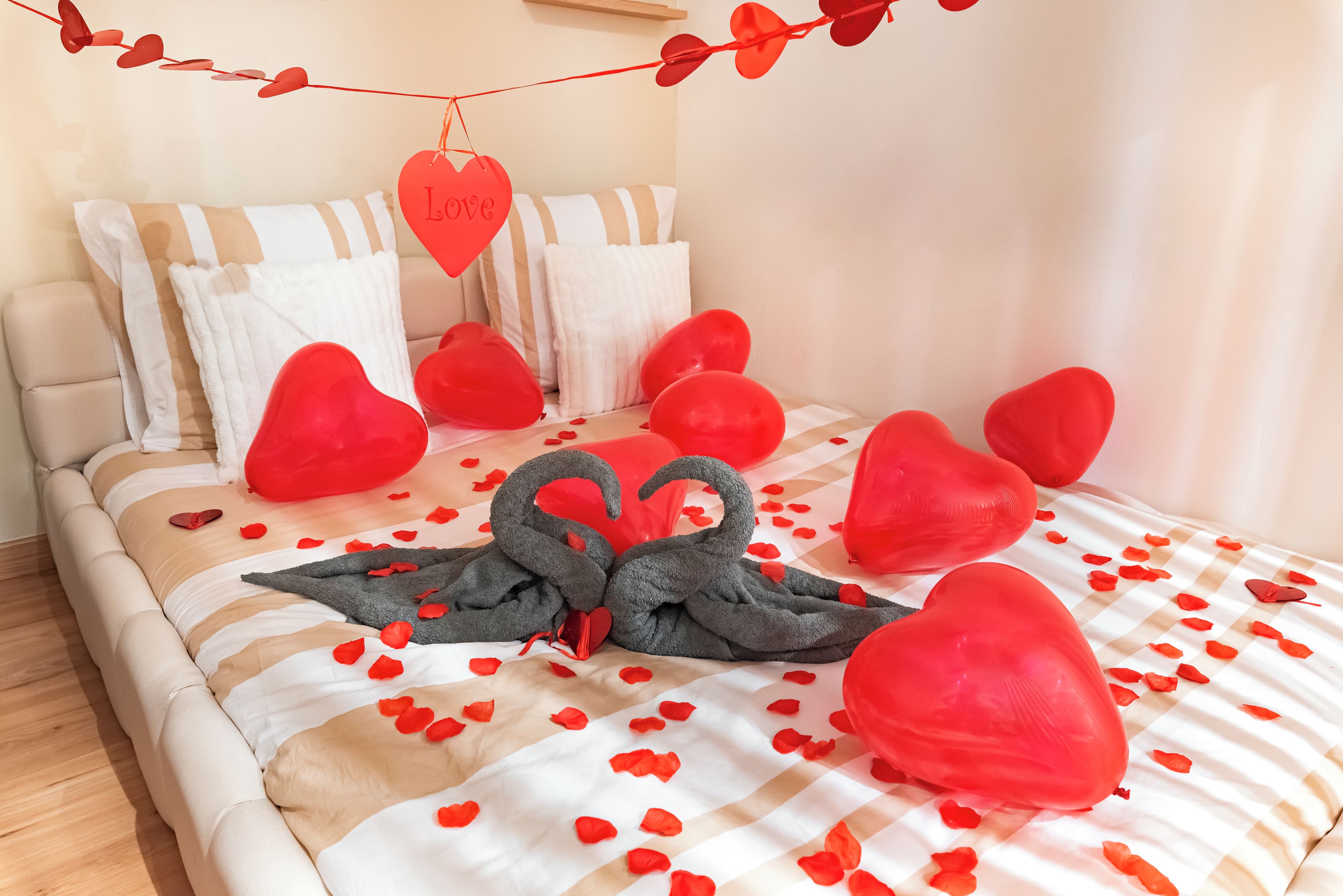 Ein Bett mit einem gestreiften Bettüberwurf, herzförmigen Kissen und roten Dekorationselementen.