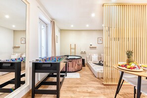 Uma sala de estar moderna com mesa de futebol, uma mesa redonda de madeira com frutas e um sofá.