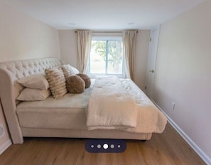 A bedroom with a large bed, a window with curtains, and a wooden floor.