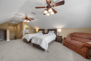 A bedroom with two beds, a ceiling fan, a brown couch, and a carpeted floor.