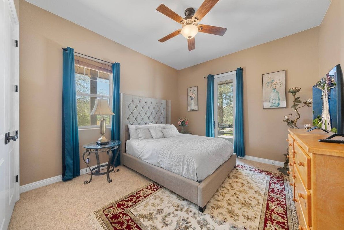 A bedroom with a bed, a ceiling fan, a nightstand, a dresser, and a window with curtains.