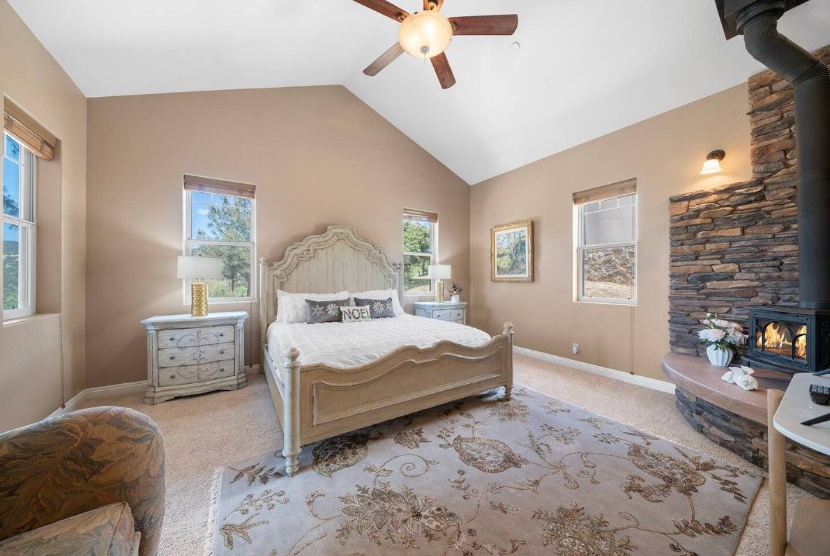 A bedroom with a bed, nightstands, a fireplace, and a ceiling fan.