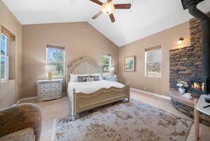 Quarto com cama, mesas de cabeceira, lareira e ventilador de teto.