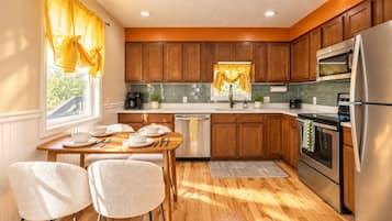 A modern kitchen with wooden cabinets, stainless steel appliances, and a dining area with two chairs.