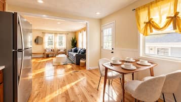 A modern kitchen with wooden flooring, a dining area with a table set for four, and a living room with a sofa and chairs.