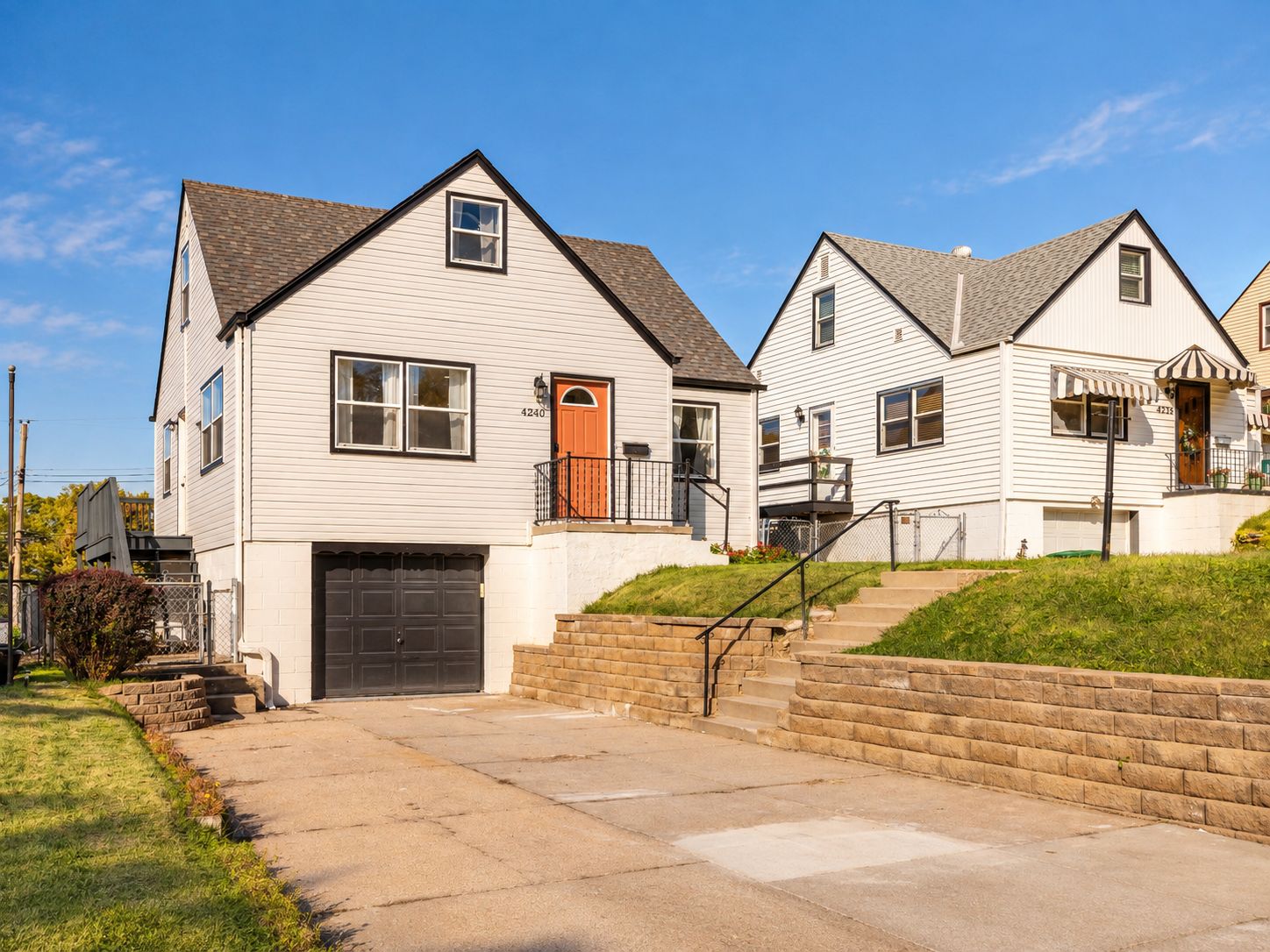 A residential area with two-story houses featuring front porches, a driveway, and a stone retaining wall.