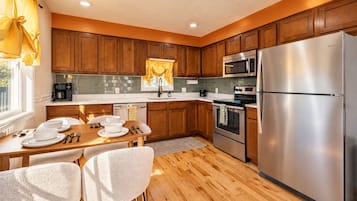 Une cuisine moderne avec des meubles en bois, des appareils en acier inoxydable et un coin repas comprenant une table et des chaises.