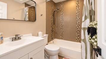 A bathroom with a white sink, toilet, and bathtub. There is a shower curtain with a checkered pattern, and a mirror above the sink.