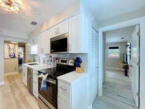 A modern kitchen with white cabinetry, a microwave, oven, and a sink. There is a painting on the wall and a door leading to another room. - Casa LUNA,charming-newly remodeled 3BR/2BA Canalfront Retreat near Siesta Beach (Sarasota)