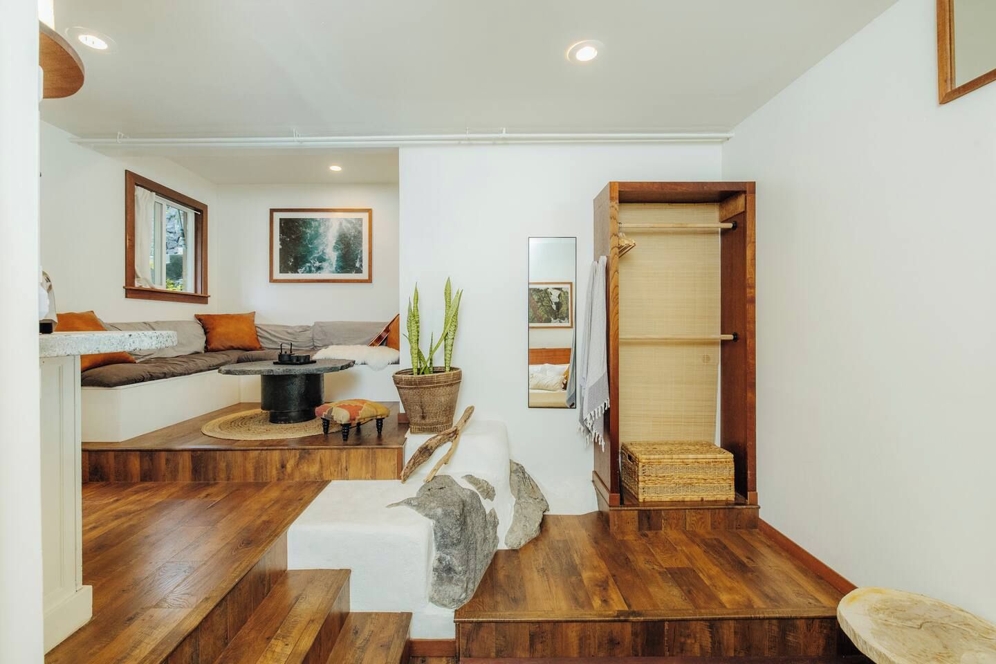 Un intérieur moderne avec un escalier en bois, un coin salon avec des coussins, une petite table avec une bouilloire et une plante en pot.