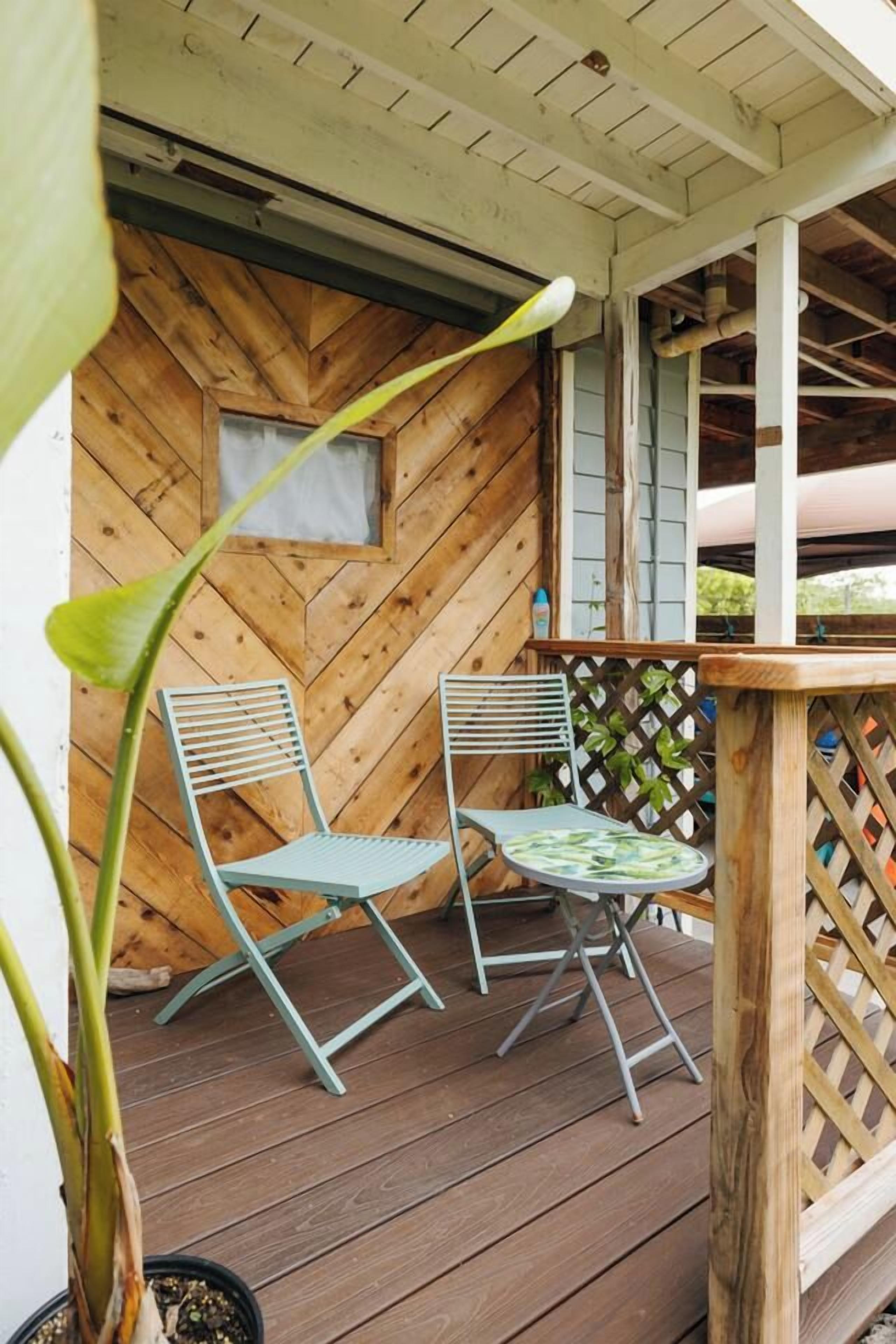 A wooden deck with two metal chairs and a small table, a wooden wall with a herringbone pattern, and a lattice fence.