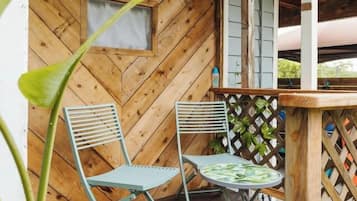 A wooden deck with two metal chairs and a small table, a wooden wall with a herringbone pattern, and a lattice fence.