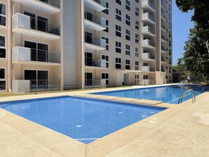 A modern apartment building with balconies, a swimming pool, and a clear sky. - Live Jaco 1207 Ocean View 2BR Condo Near Beach (Jaco)