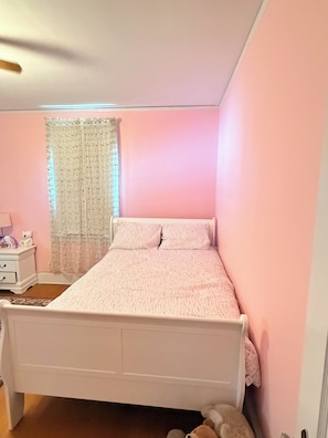A bedroom with a single bed, a nightstand, a lamp, a window with curtains, and a teddy bear on the floor. - Cozy Home in Serene Orange walking distance to town! (Orange)