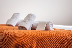 A neatly folded white towel with a tag on a textured orange blanket. - Sutherland Apartments - Apt 26 (London)