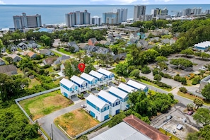 An aerial view of a residential area with a cluster of blue and white buildings, surrounded by greenery and a coastline in the background. - The Blue Sky 2 Blocks to Beach Pets (Myrtle Beach)