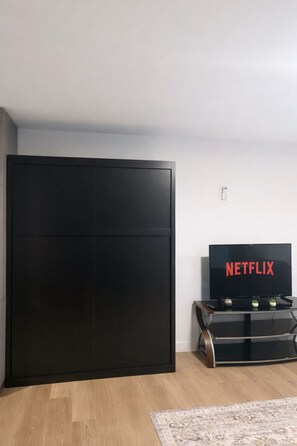 Une pièce avec une armoire noire, un téléviseur à écran plat orné du logo Netflix et une petite table agrémentée d’objets décoratifs.