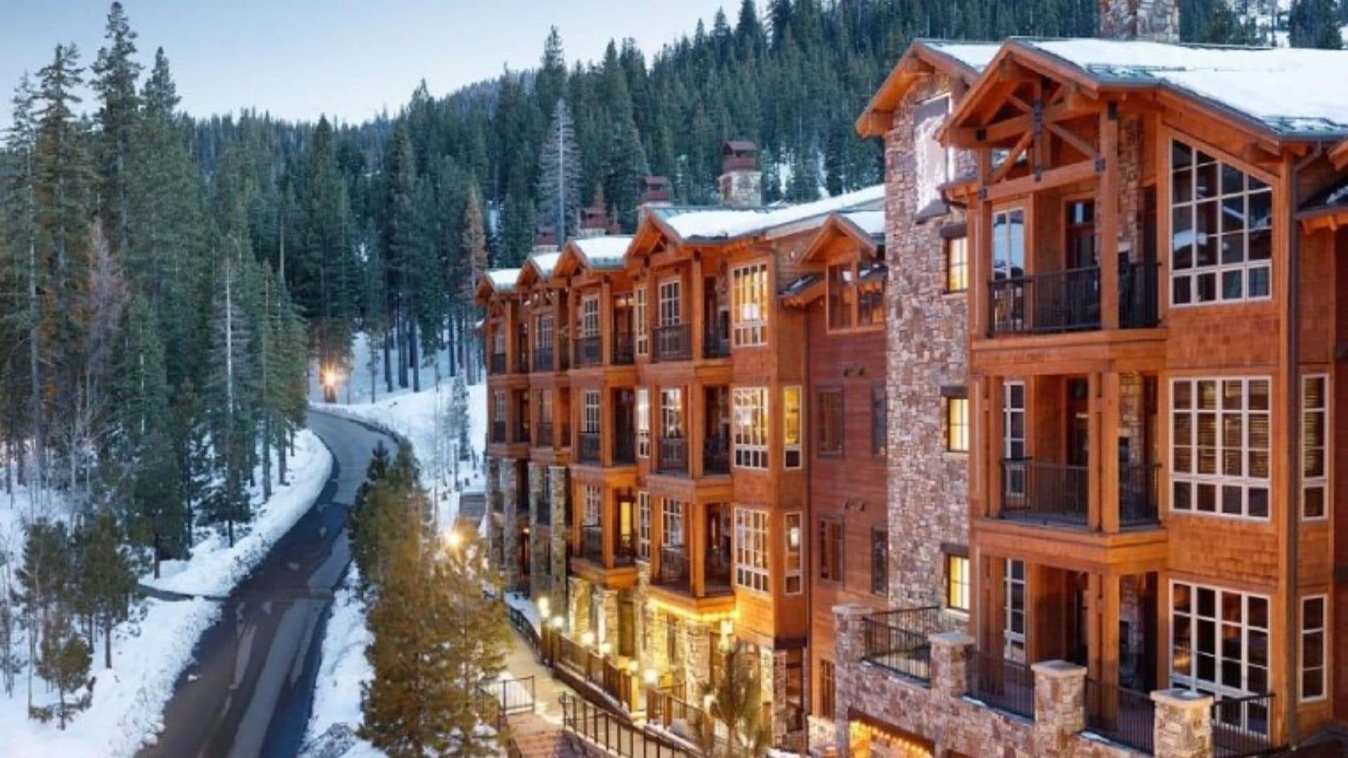 A multi-story lodge with a stone facade and large windows, surrounded by a snowy forest.