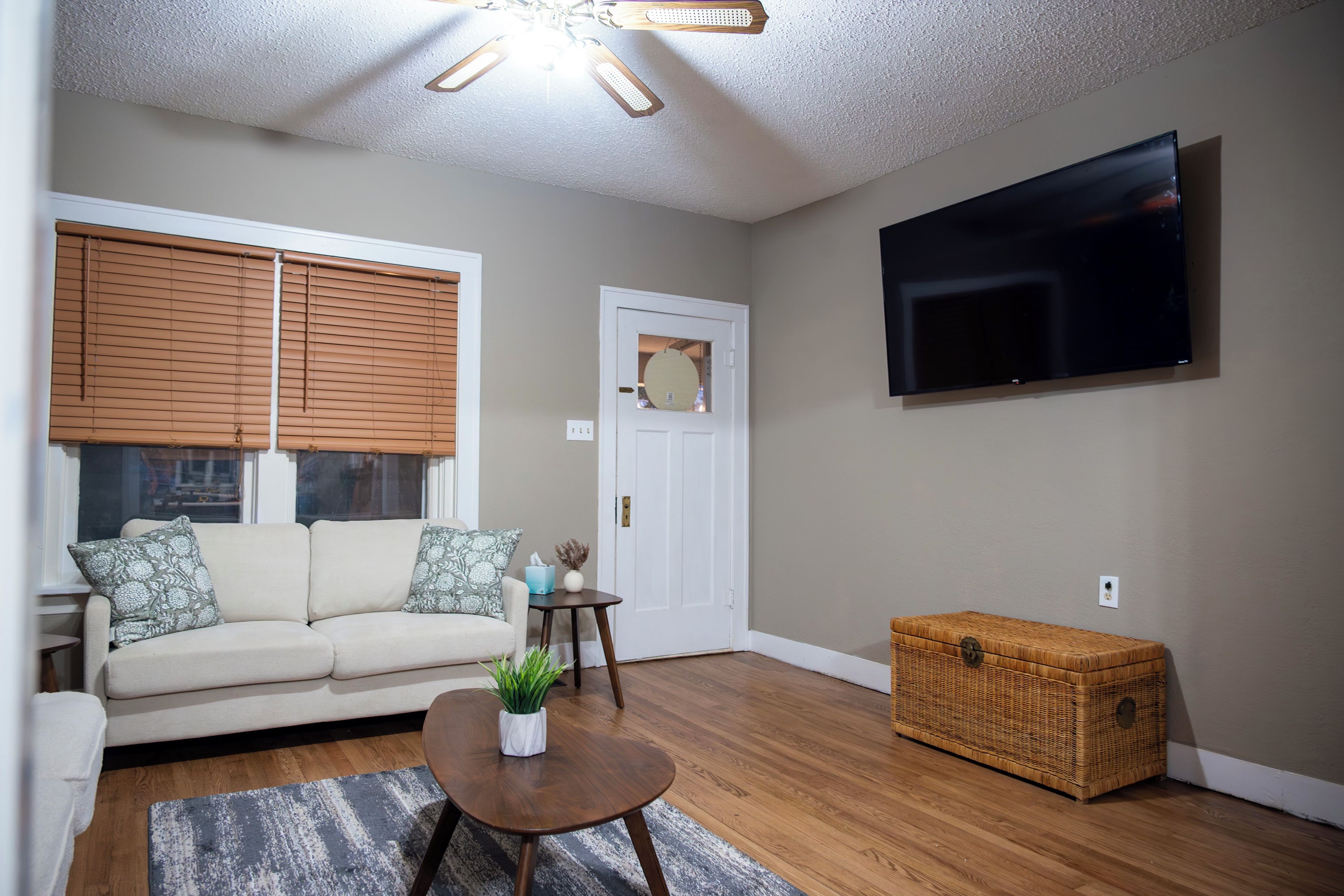 A living room with a sofa, a coffee table, a television, a wicker chest, and a door.
