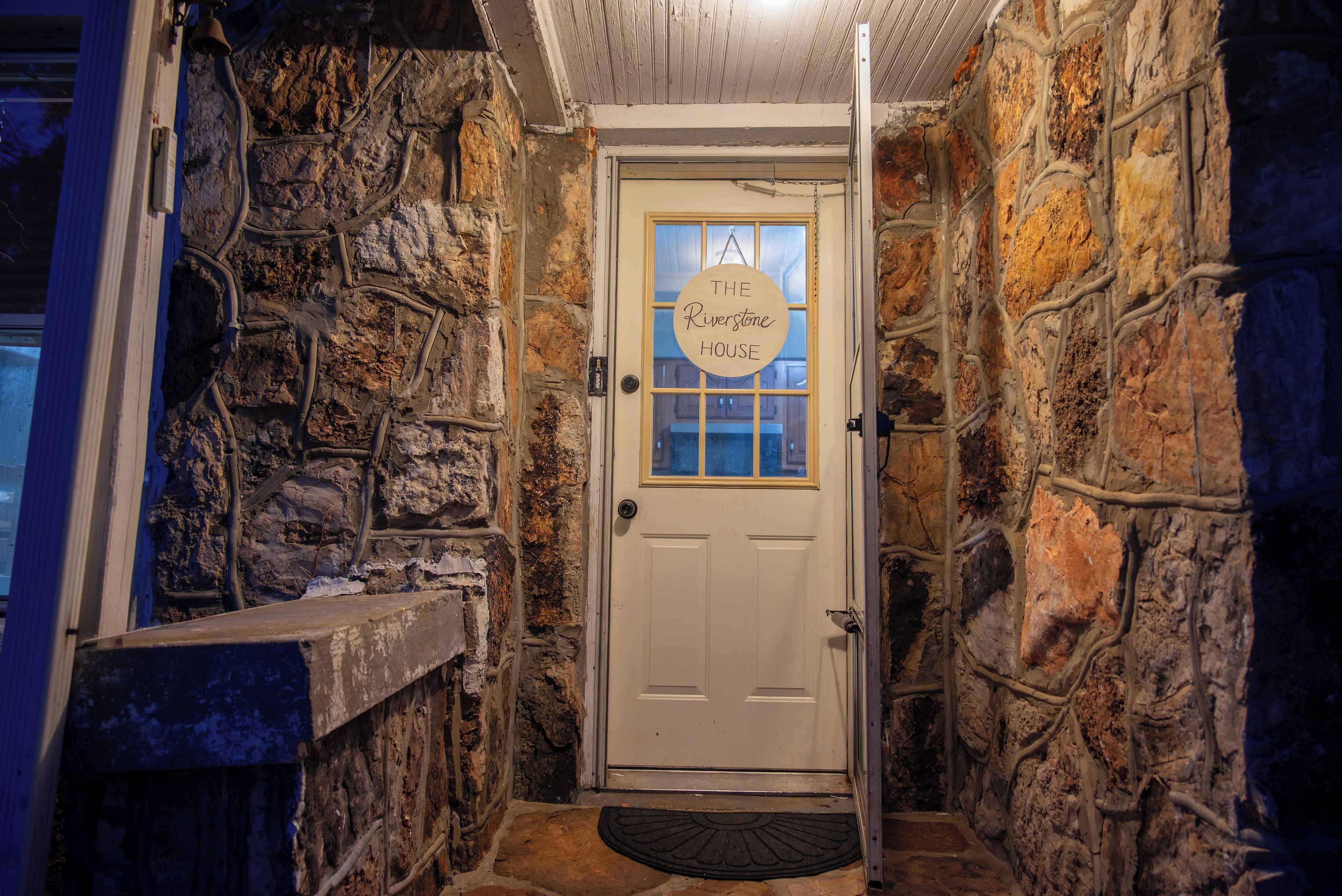 A stone-walled hallway leading to a door with a sign reading 'The Riverstone House.'